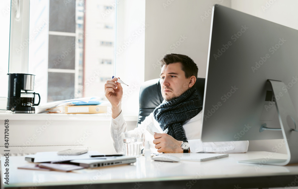 A young freelancer, businessman or office worker has a cold and flu. A man holds a thermometer in his hand, a high temperature with SARS. Epidemic of influenza or coronavirus. Sick at work