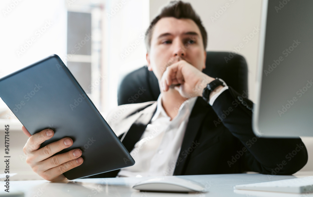 Young successful businessman and office employee reading news on his tablet. Coffee break during the working day. A financial analyst or broker studies stock market fluctuations. Economic crisis 2020 Young successful businessman and office employee reading news on his tablet. Coffee break during the working day. A financial analyst or broker studies stock market fluctuations. Economic crisis 2020