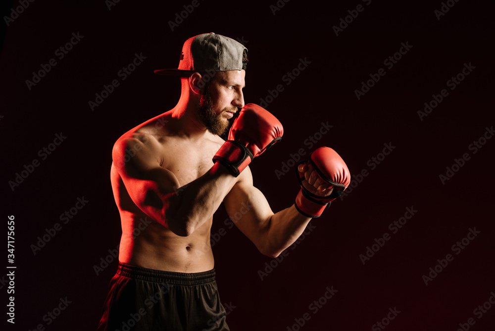 Young muscular man looking aggressive with boxing gloves on black background