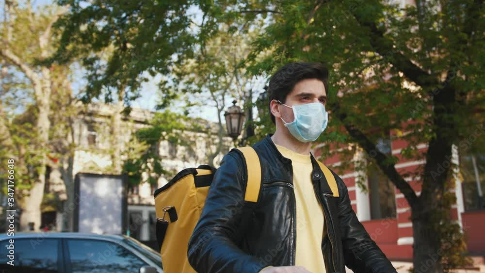 Portrait of delivery man with yellow bagpack and protective mask standing with electric scooter in the city, slow motion Portrait of delivery man with yellow bagpack and protective mask standing with electric scooter in the city, slow motion