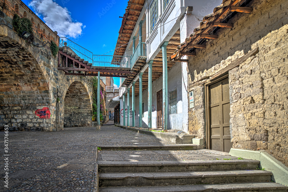 Old house in front of the ancient and famous stone Puente Roto, or Broken Bridge, on a sunny afternoon, Cuenca, Ecuador.