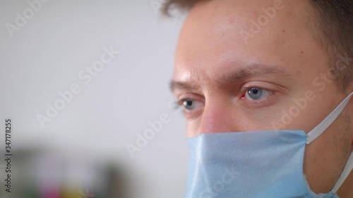 A tired doctor in medical mask opens his eyes and slowly raises them. Close-up portrait. Man in medical mask.