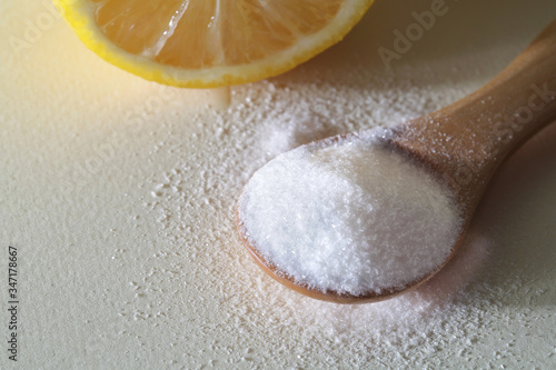 powdered Vitamin C on wooden spoon with cut lemon on white background