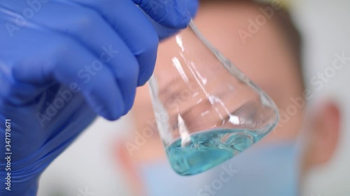 Doctor in blue gloves and medical mask picks up and turns a flask of liquid. The development of antiseptic.
