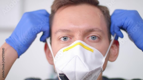 Young medic in blue gloves puts on a respirator. Protector of people. Protection from coronovirus and disease.