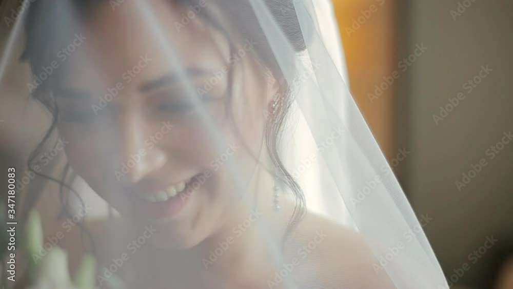 Happy beautiful european bride in an elegant wedding dress and veil holds a bouquet of colorful flowers and laughs with happiness in the hotel room in the morning. Woman is preparing for the wedding. Happy beautiful european bride in an elegant wedding dress and veil holds a bouquet of colorful flowers and laughs with happiness in the hotel room in the morning. Woman is preparing for the wedding.
