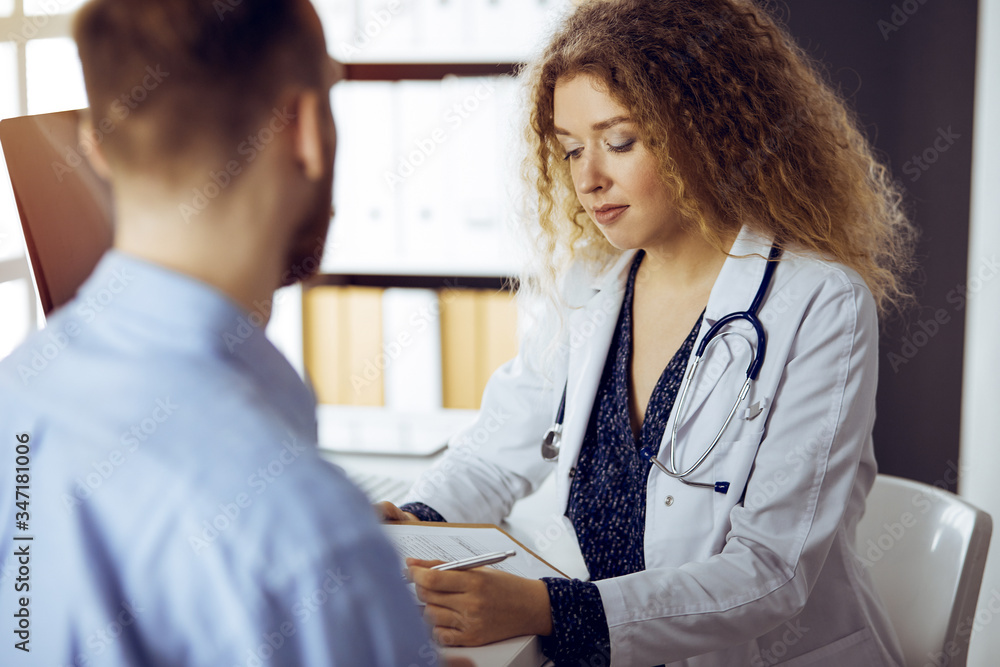 Fototapeta premium Female doctor and male patient discussing current health examination while sitting in sunny clinic. Medicine concept