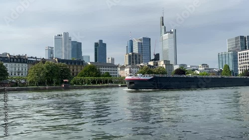 Frankfurt, Germany - 08th May 2020: A german photographer visiting the city, taking a video of a huge container ship drivers on the river Main with the skyline in the background.