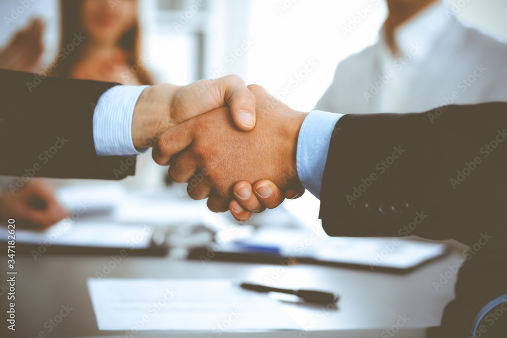 Business people shaking hands at meeting while theirs colleagues clapping and applauding. Group of unknown businessmen and women in modern white office. Success teamwork, partnership and handshake Business people shaking hands at meeting while theirs colleagues clapping and applauding. Group of unknown businessmen and women in modern white office. Success teamwork, partnership and handshake