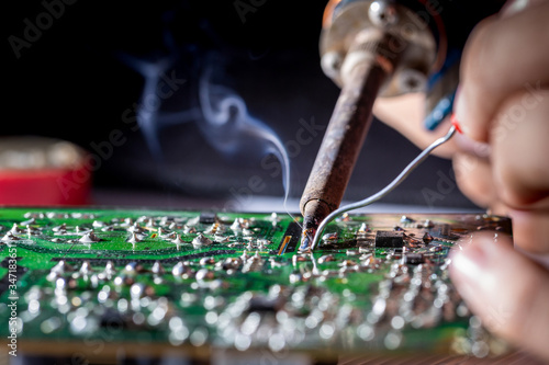 Bild auf Leinwand Technician repairs circuit board of television with iron soldering and tin wire,
