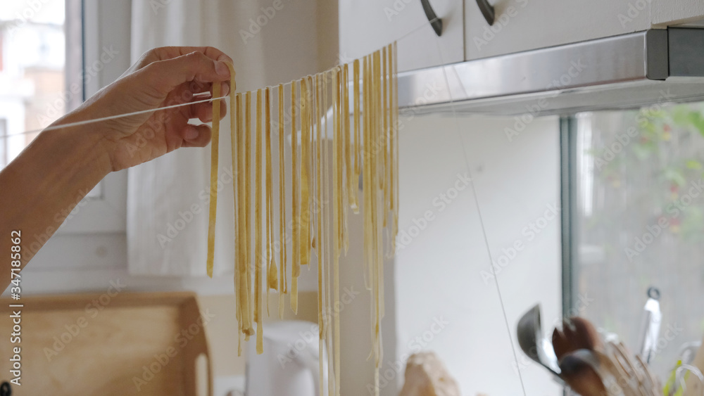 une personne fait sécher des pâtes fraiches sur un fil dans une cuisine Stock Photo Adobe Stock
