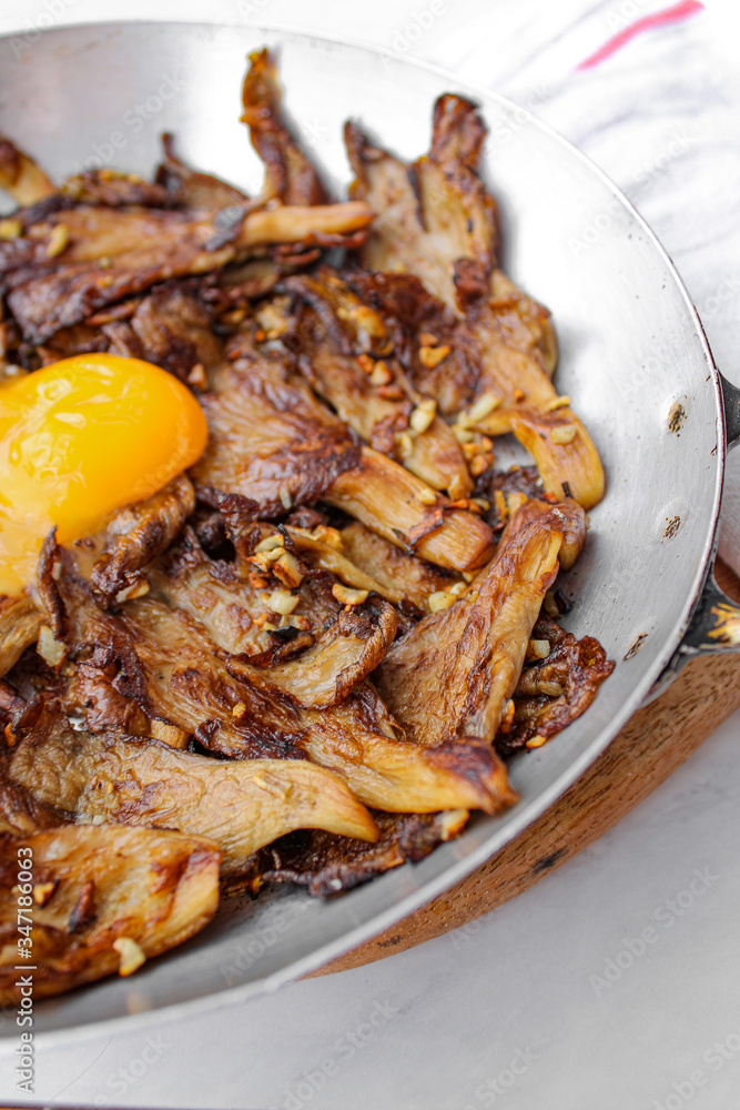 Sautéed oyster mushrooms with garlic and topped with egg yolk. Oven roasted in grey baking tray. Flat lay. Tope view. Sautéed oyster mushrooms with garlic and topped with egg yolk. Oven roasted in grey baking tray. Flat lay. Tope view.