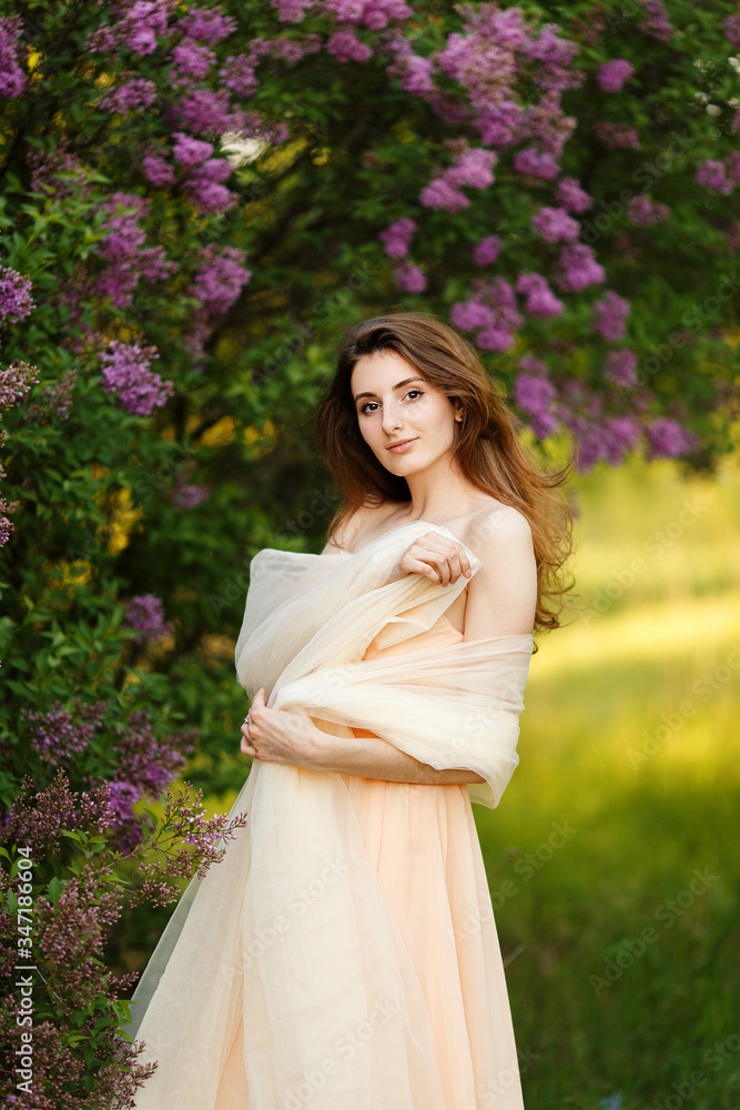 Romantic portrait of young beautiful girl standing in spring lilac garden