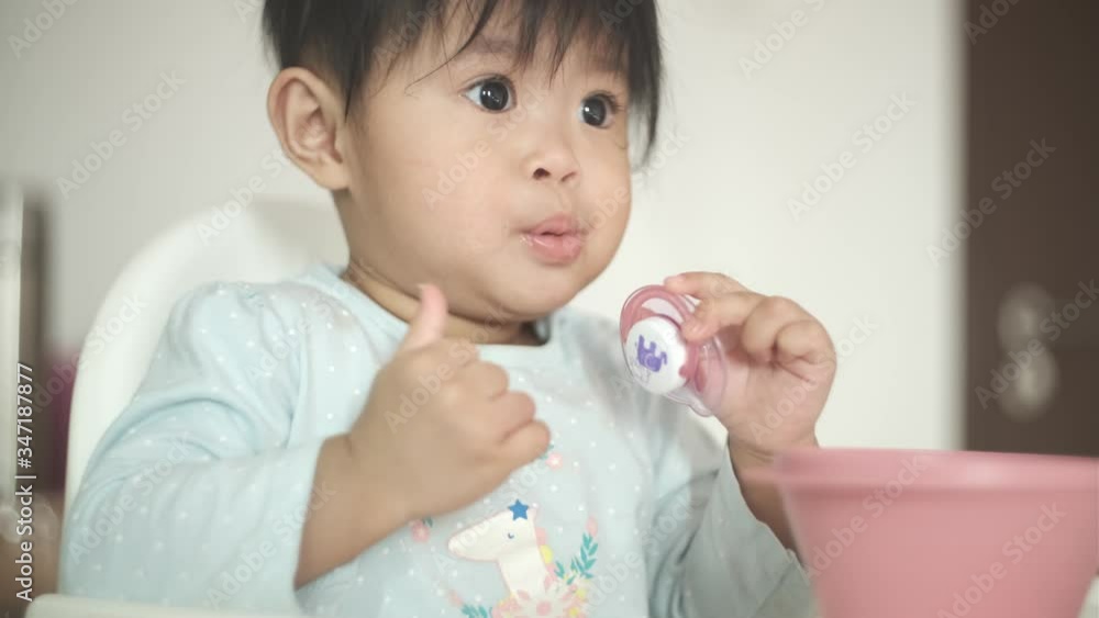 Baby eating biscuit snack from plastic bowl on baby chair Baby eating biscuit snack from plastic bowl on baby chair