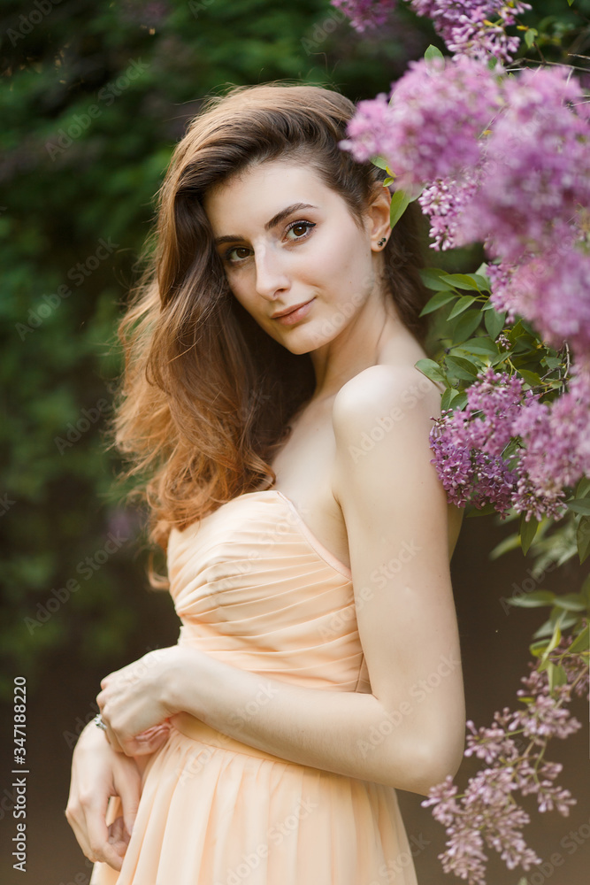 Romantic portrait of young beautiful girl standing in spring lilac garden