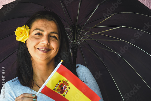  Woman with umbrella holds flag of Spain in front of isolated wall background