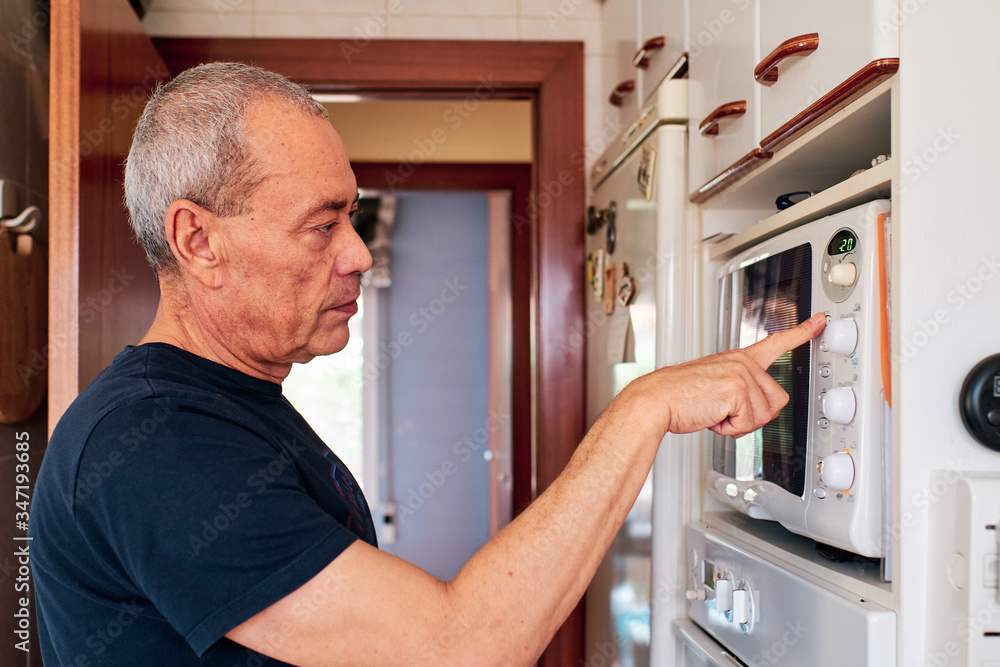 Old man with grey hair using the microwave oven in his kitchen Old man with grey hair using the microwave oven in his kitchen