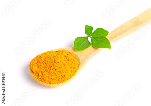 Top view isolated wooden spoon with turmeric powder and green leaves.