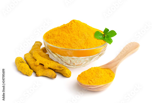 Turmeric powder in glass bowl with green leaves, dry roots and wooden spoon isolated on white background.