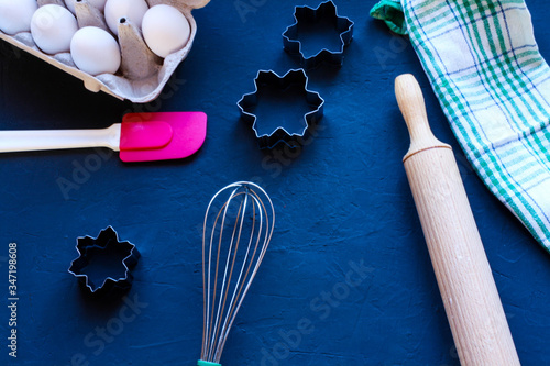 Baking utensils and ingredients are spread out on the dark surface.