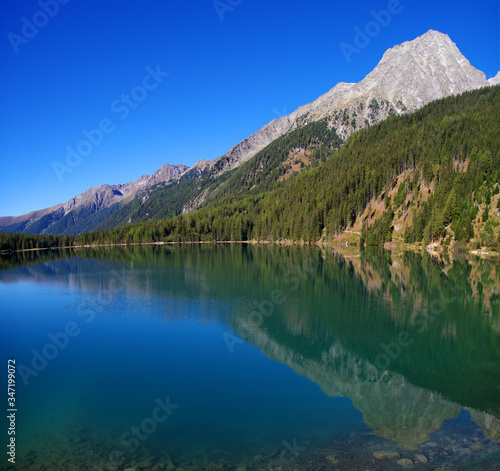Fototapeta Naklejka Na Ścianę i Meble -  bright blue mountain lake under blue sky with woods, stones and snow