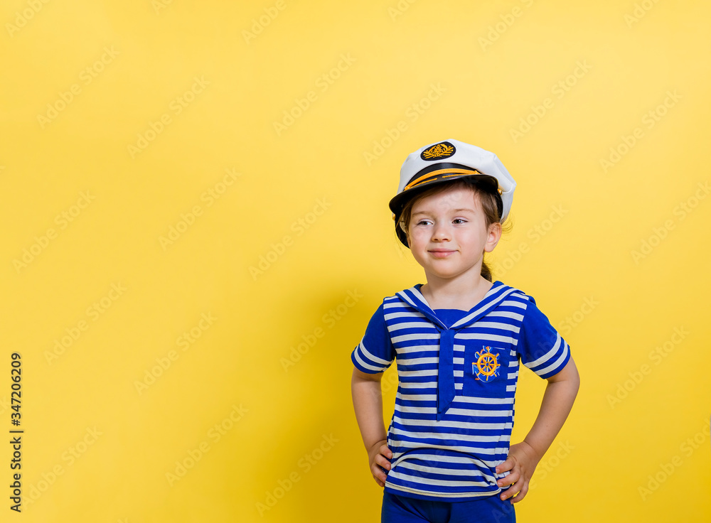 A little sailor girl on a yellow background looks away. A girl in a sailor suit and a cap on an isolated background with copy space A little sailor girl on a yellow background looks away. A girl in a sailor suit and a cap on an isolated background with copy space