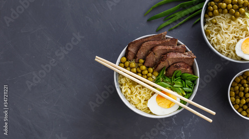Asian traditional soup in a bowl on grey background. Beef pho bo with eggs and green peas. Copy space.
