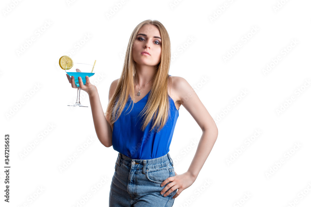 A girl looks haughty in bright blue jeans and a blouse with a blue cocktail with lemon. Young lady resting with alcohol A girl looks haughty in bright blue jeans and a blouse with a blue cocktail with lemon. Young lady resting with alcohol