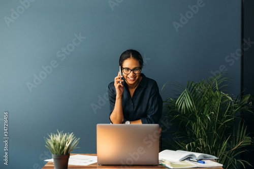 Young businesswoman standing leaning to a chair in living room while talking on cell phone photo