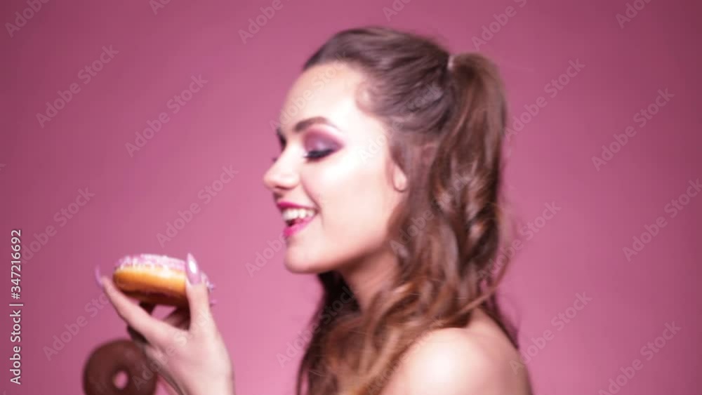 Young sexy woman eating donuts. Studio shot on pink background.