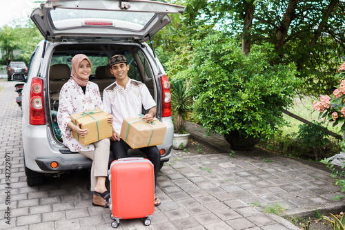 muslim couple travelling by car. man and woman sitting in the car trunk holding suitcase
