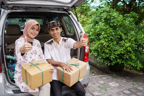 muslim couple travelling by car. man and woman sitting in the car trunk holding suitcase showing thumb up