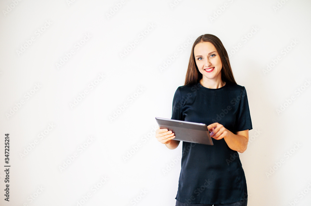 A young woman in black wear with a digital tablet, she is watching on the camera with a smile. Concept of technology, digitalization. Isolated on white background. Copy space A young woman in black wear with a digital tablet, she is watching on the camera with a smile. Concept of technology, digitalization. Isolated on white background. Copy space