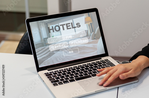 ホテルのオンライン予約検索のイメージ　ノートパソコンでホテルの予約検索の画面を見せている女性の手