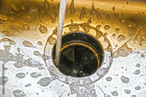 Water running into a garbage disposal of a stainless steel sink with gold toned blurred background and sharp silver foreground with soap bubbles draining toward hole photo