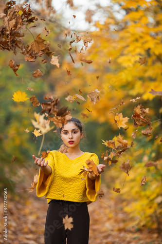 Fototapeta Naklejka Na Ścianę i Meble -  young girl throws yellow leaves into the air