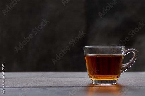 Close up hot tea cup on wood table . hot tea in handle glass with copy space for text or design. Hot tea with raw mortar background.