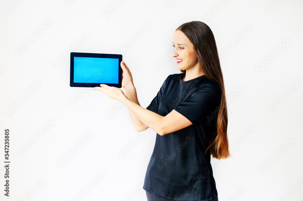 Beautiful girl in black t-shirt is holding a blank digital tablet in hands and looks at it, copy space for text, isolated on a white background