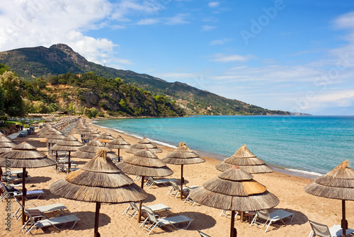 Row of Straw umbrellas and lounges at sandy beach Zakynthos, Greece.