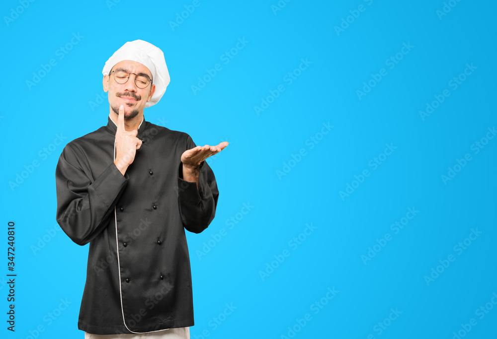 Doubtful young chef holding something with his hand Doubtful young chef holding something with his hand