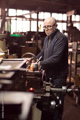 A man 50-60 le works at the machine at the factory. Man with glasses. Hard work.