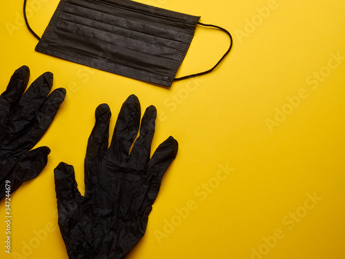 Sterile black glove and black protective medical mask, yellow background, copy space