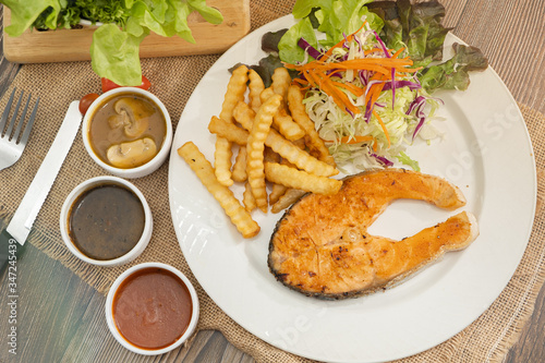 Grilled salmon steak with french fries and fresh salad on sackcloth and wooden table background. Ready to eat food. Copy space.