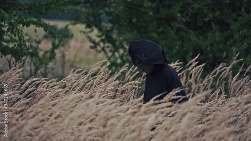 Scary figure with horrorful face outdoors. Ghost in black cloak walking in wheat field. Spooky death among nature. Halloween concept. photo