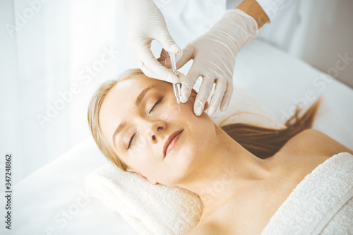 Beautician doctor doing beauty procedure with syringe to blonde female face. Cosmetic medicine, beauty injections concept