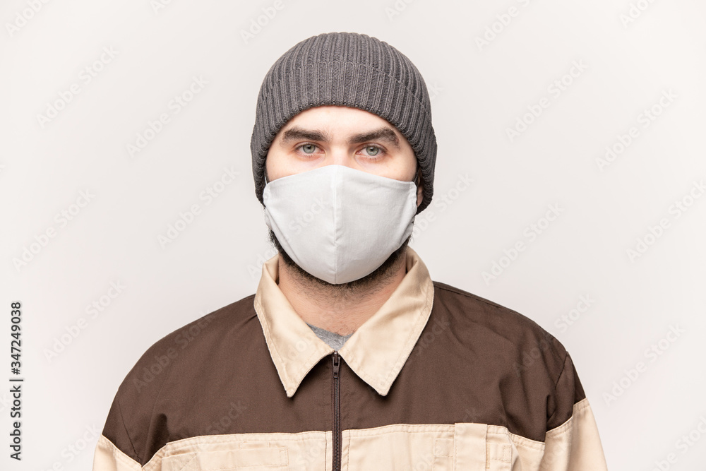 Young man in beanie cap, workwear and protective mask looking at you Young man in beanie cap, workwear and protective mask looking at you
