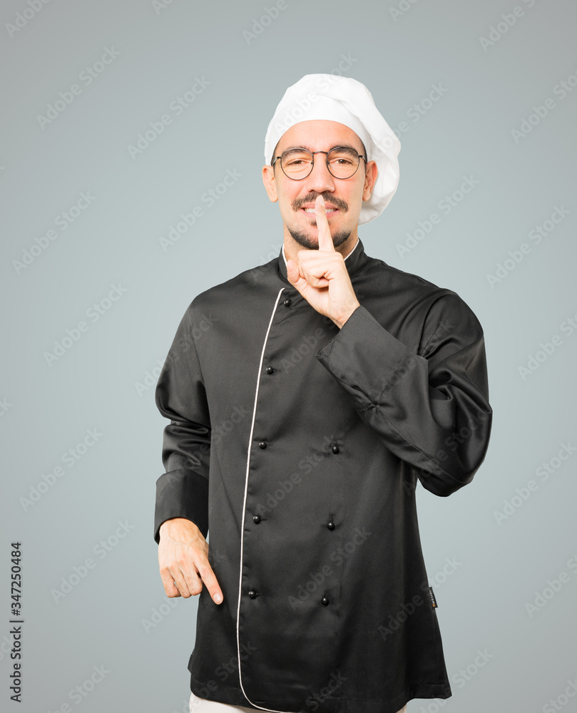 Happy young chef asking for silence gesturing with his finger Happy young chef asking for silence gesturing with his finger