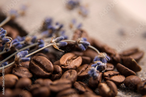 Coffee beans close-up, spilled on the table. Coffee beans on a background of burlap, decorated with branches of dried lavender. Beautifully blurred background. Macro photo.