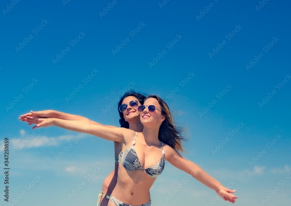 two young women relaxing on the beach. Two charming teen friends in bright swimsuits against the sky. Copy space