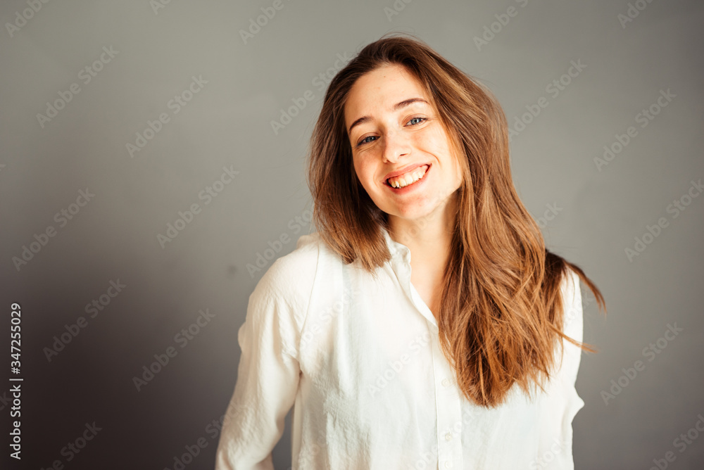 Smiling girl with a satisfied face hands near the face on a gray background, close-up. Nude makeup, without retouching. Smiling girl with a satisfied face hands near the face on a gray background, close-up. Nude makeup, without retouching.